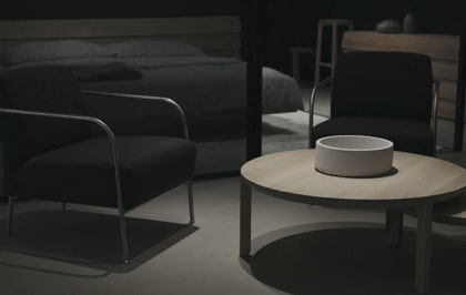 A dimmly lit living room setup with a black chair in next to a low white wood table.